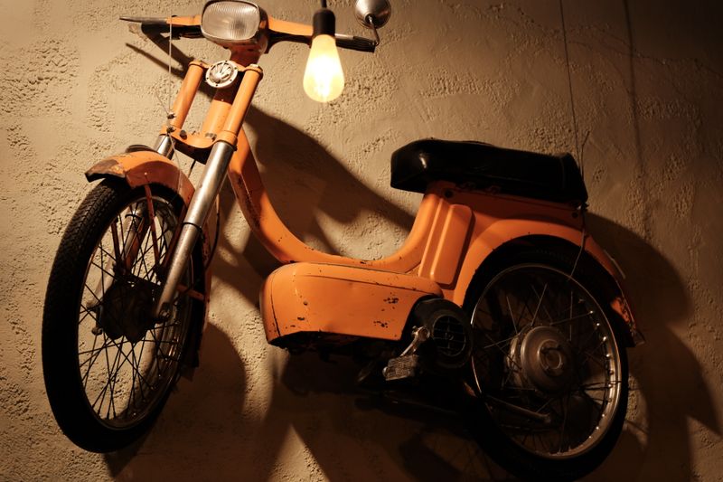 Oranje bromfiets tegen een warm verlichte muur