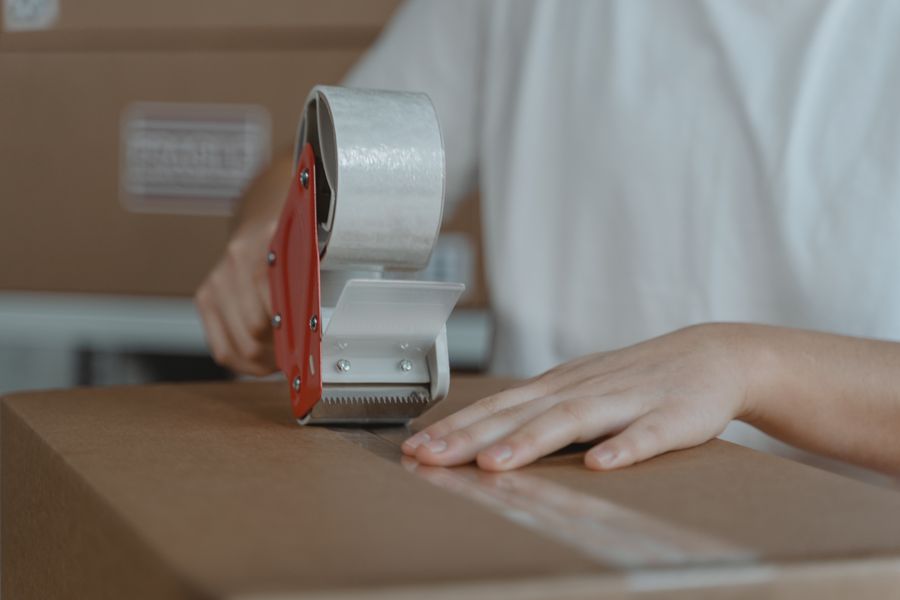 Handen plakken een kartonnen doos dicht met tape